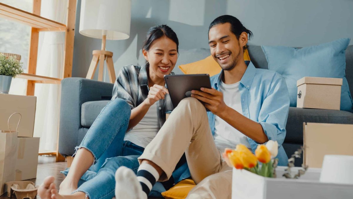 Happy couple house hunting and reviewing their cryptocurrency portfolio on a laptop, symbolizing new mortgage rules for crypto investors