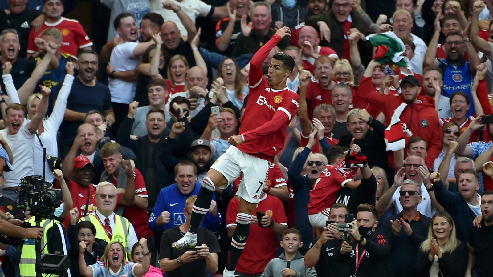 Manchester United fans in a stadium waving red scarves and holding up smartphones, representing the blend of club tradition and digital technology.