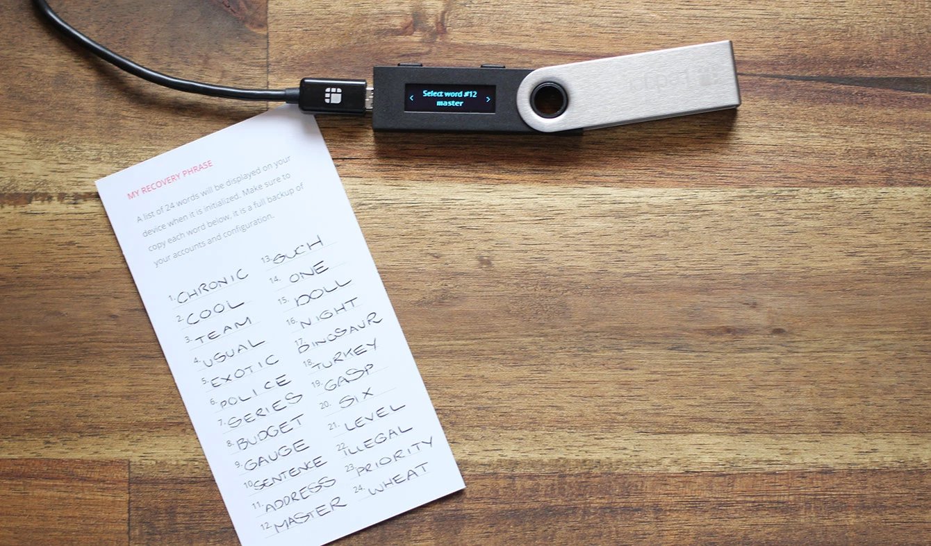 Side-by-side comparison of a handwritten crypto seed phrase on paper and a Ledger Recovery Key card for secure wallet backup