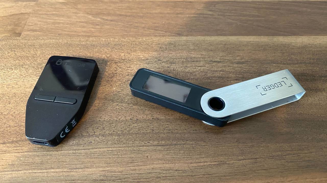 Side-by-side comparison of Trezor Safe 3 and Ledger Nano X hardware wallets on a desk