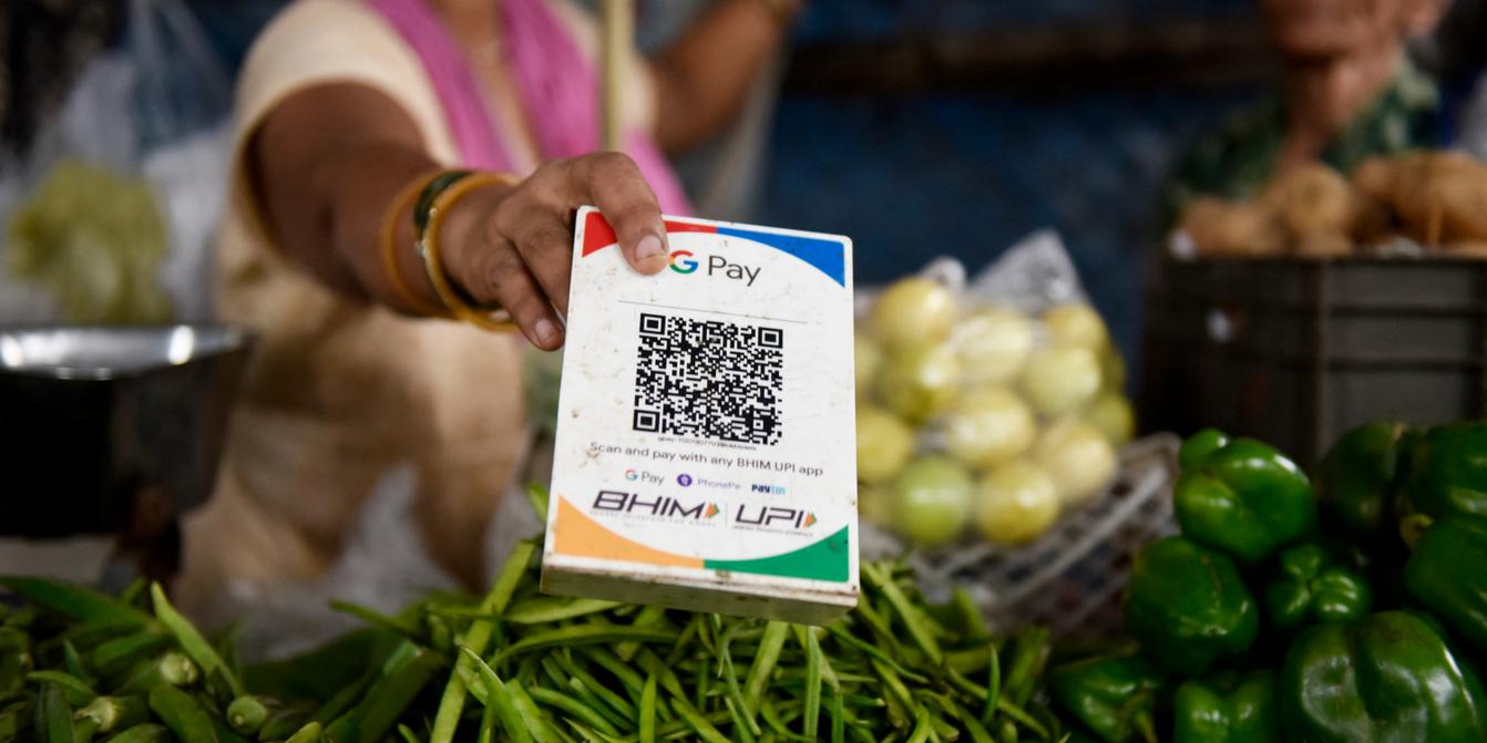 Street vendor in bustling Asian market stall displaying printed USDT QR code for offline crypto payments