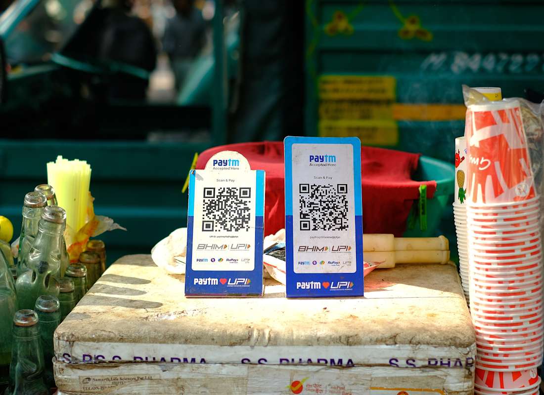 Street vendor in bustling market holding printed USDC QR code for offline stablecoin payments