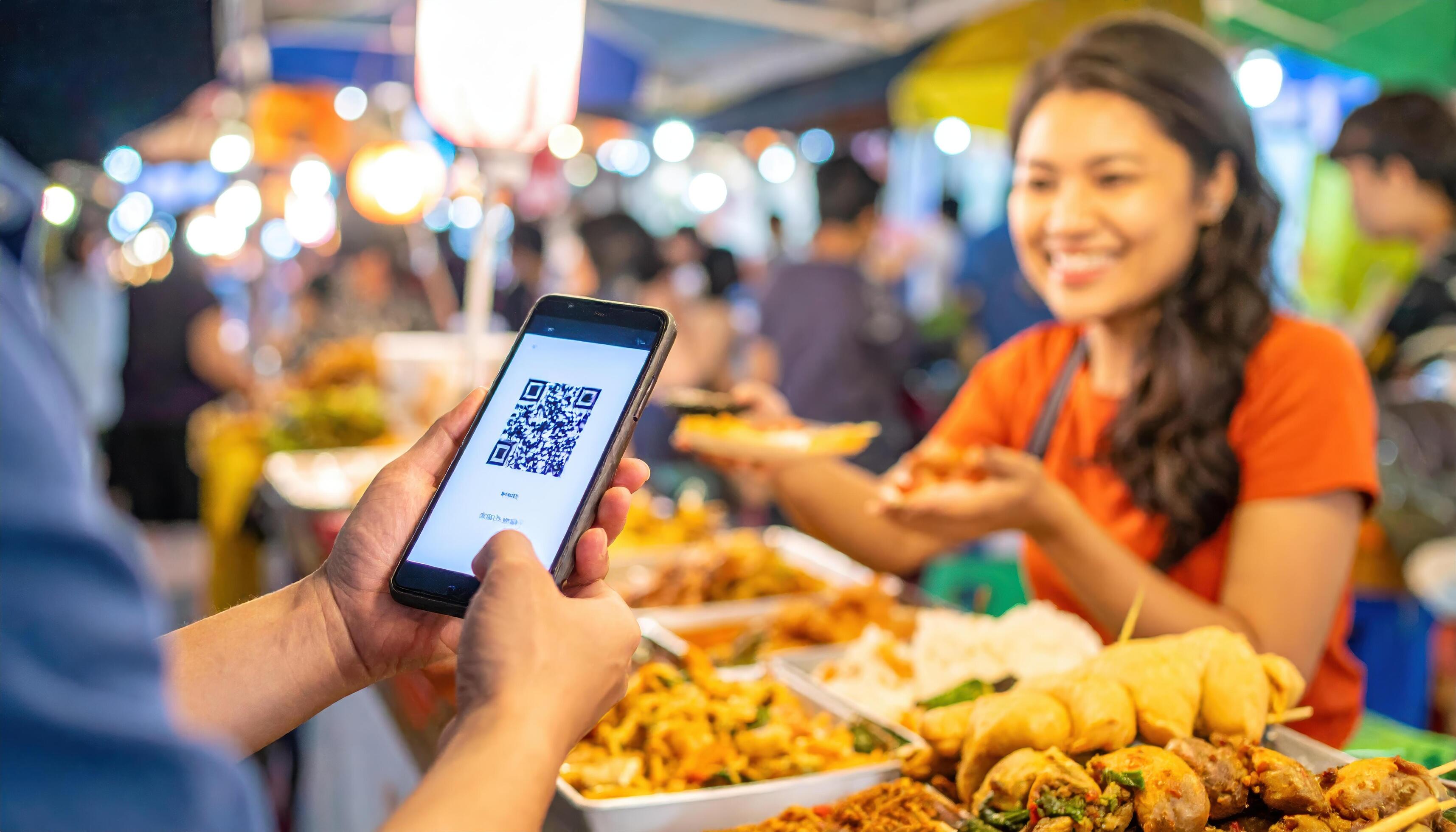 Thai street vendor in vibrant night market scanning USDC QR code payment with customer smartphone, offline stablecoin crypto acceptance Thailand